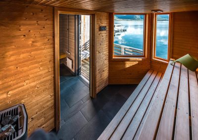 Sauna interior with wooden benches and a window looking out over the sea.