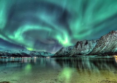 Northern lights glowing green over a calm body of water at night.