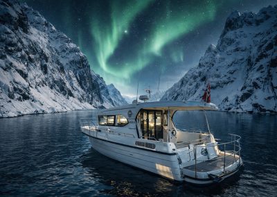 Fishing boat on the water with northern lights over snowy mountains at night.