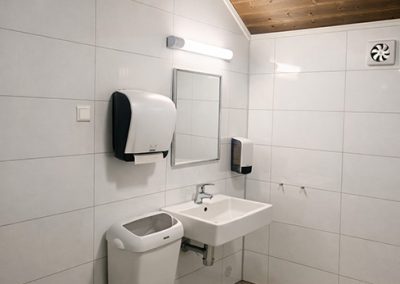 Bathroom with a toilet, sinks, and wall tiles, with a wooden ceiling.